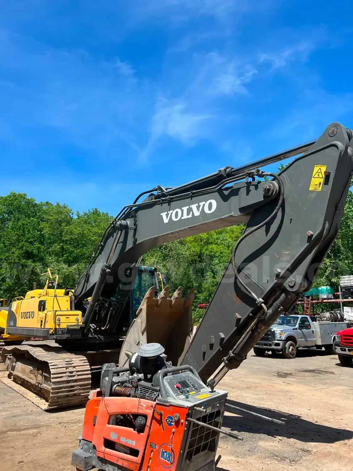 Large Volvo excavator with orange compact equipment in the foreground at an equipment yard