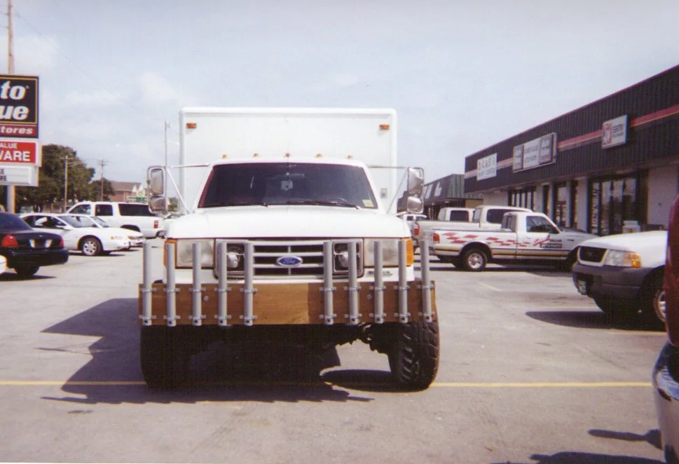 A white 4x4 ambulance with a box body and oversized off-road tires parked in a store lot