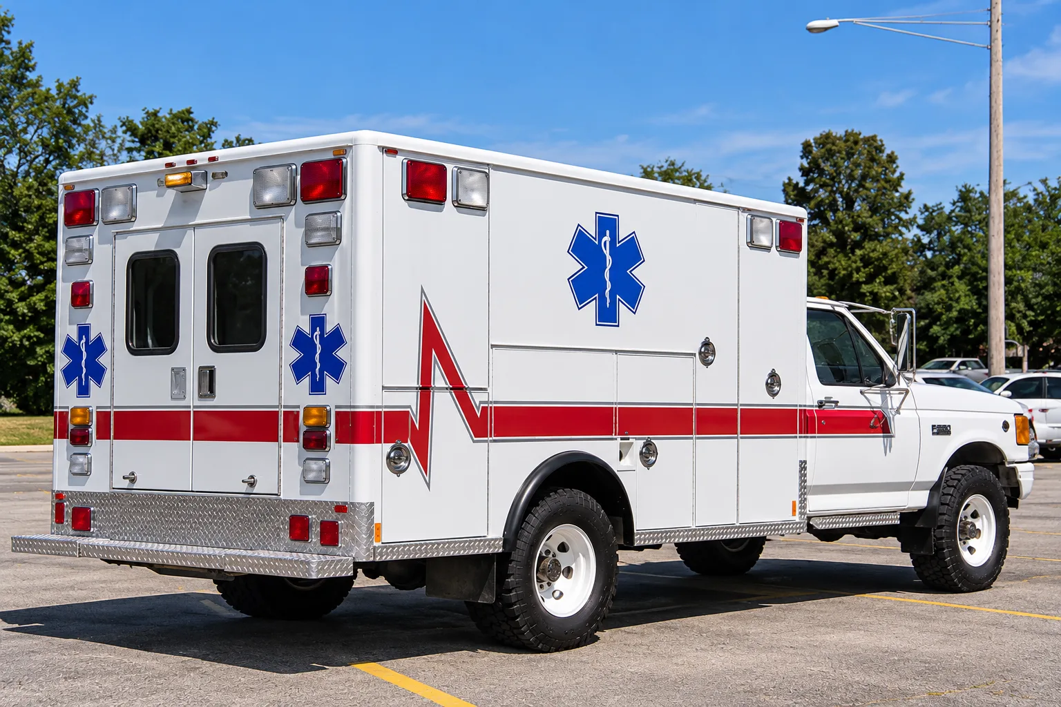 A white 4x4 Ford ambulance with red stripes and blue Star of Life emblems seen from the rear