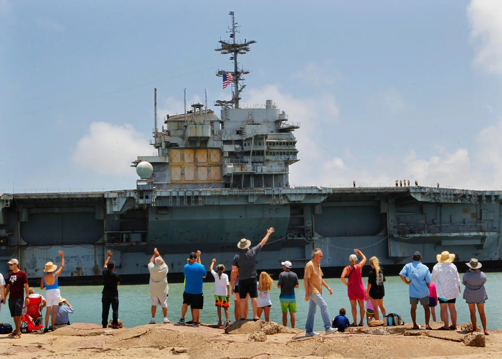 Crowds wave from the jetty as a retired aircraft carrier arrives in South Texas