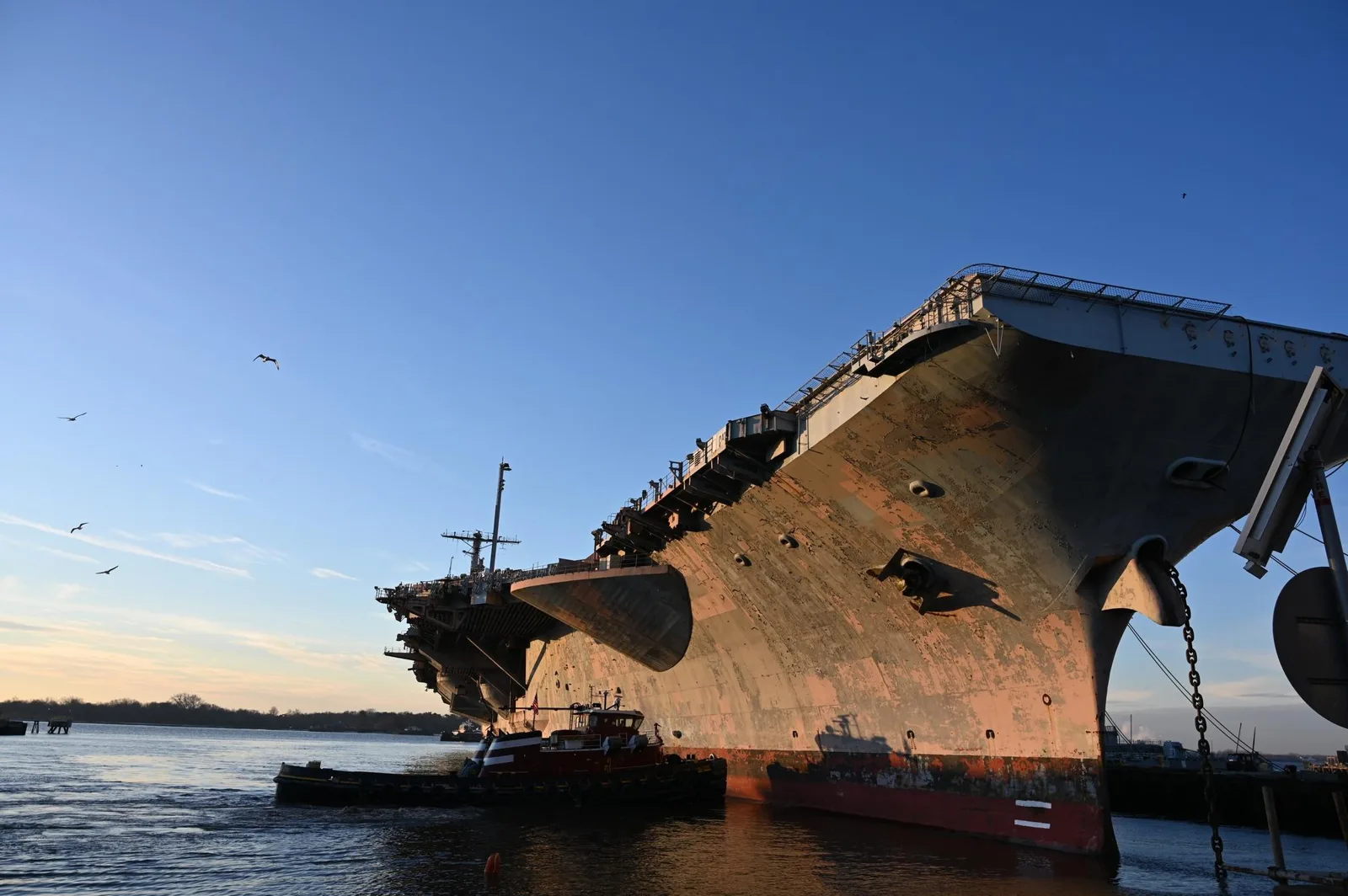 A retired aircraft carrier with a tugboat alongside at sunrise in Philadelphia