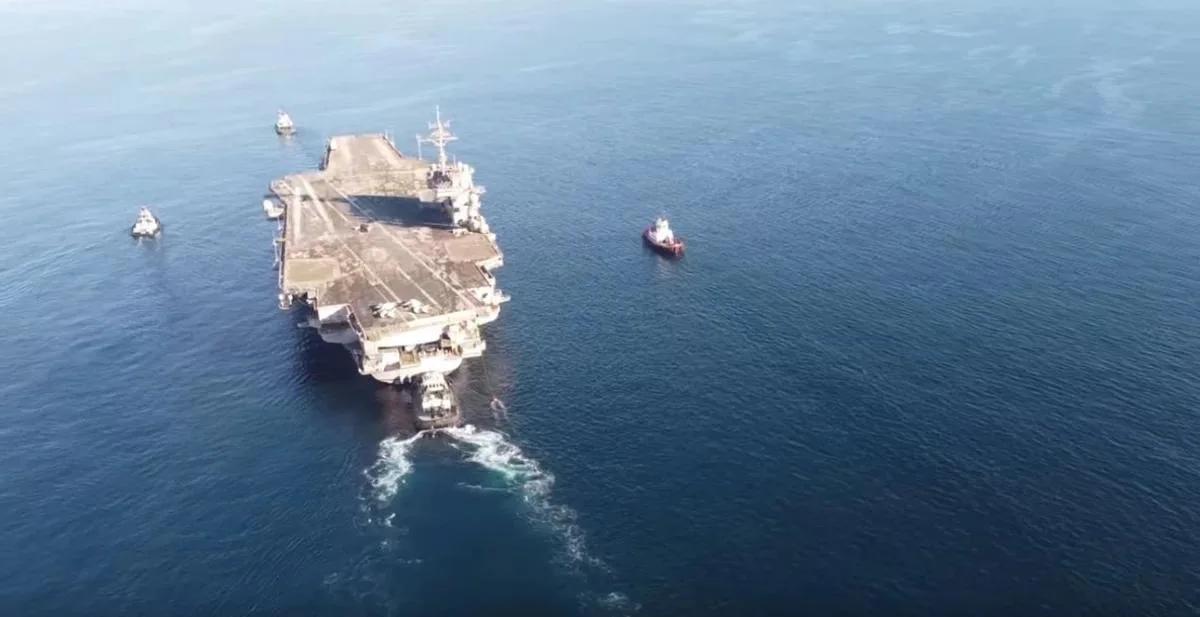 A retired aircraft carrier under tow with tugboats alongside