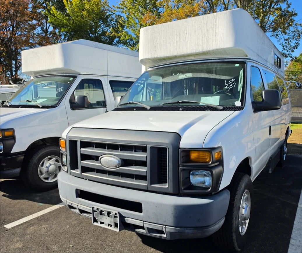 A white high-top Ford E-Series van in the Delaware Surplus Services yard, with a second one beside it.