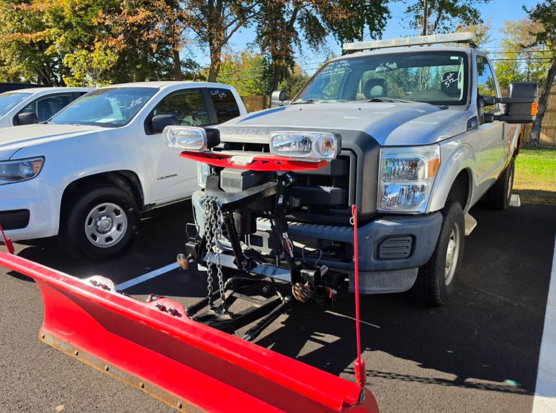 A silver Ford Super Duty pickup with a red snow plow mounted on the front in the Delaware Surplus Services yard.