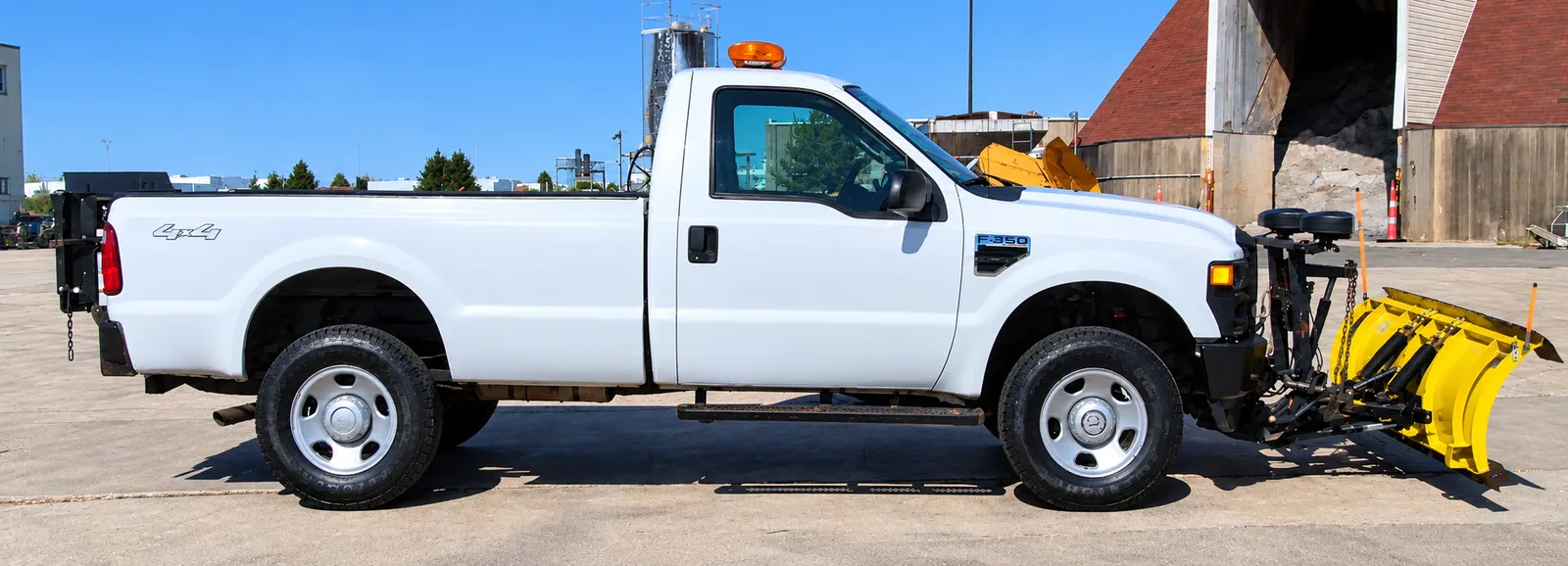 The same Ford F-350 from the passenger side, with the plow raised and the salt pile behind it
