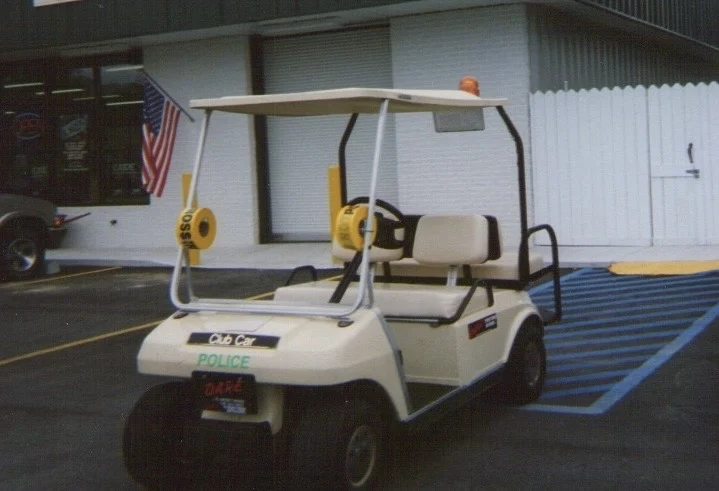 A white Club Car golf cart with an amber light on its roof parked outside a building