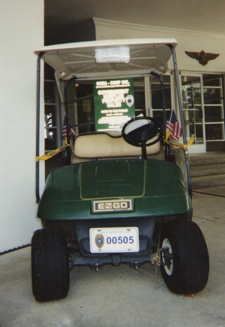 A green EZ-GO golf cart with a public safety license plate parked at an entrance