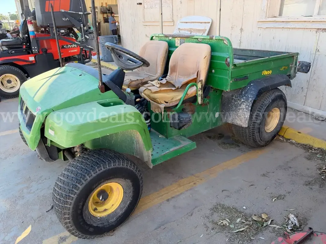 A green John Deere Gator utility vehicle with a cargo bed, parked beside a commercial mower