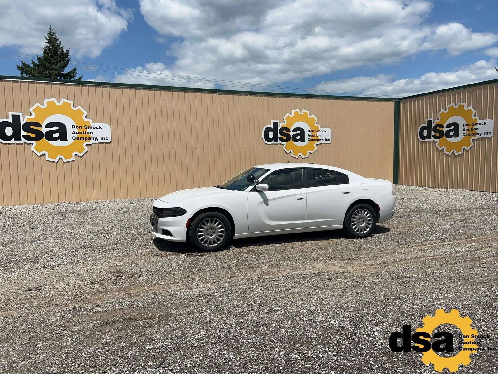 A white 2020 Dodge Charger Pursuit, retired from the Indiana State Police, parked on the gravel in front of the Don Smock Auction Company building in Pendleton.