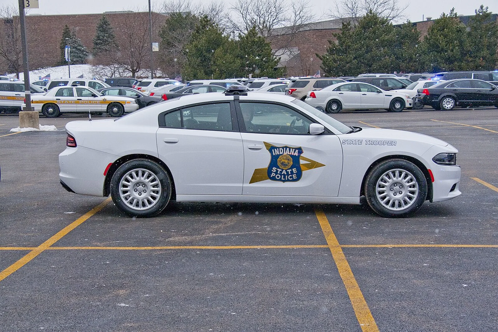 A white Indiana State Police Dodge Charger Pursuit, side view, in a lot full of state police cars.