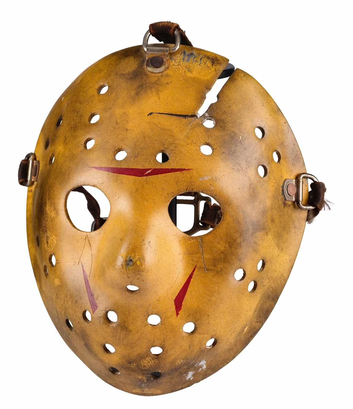 A yellowed Jason Voorhees hockey mask with red triangles, leather straps and a crack across the forehead