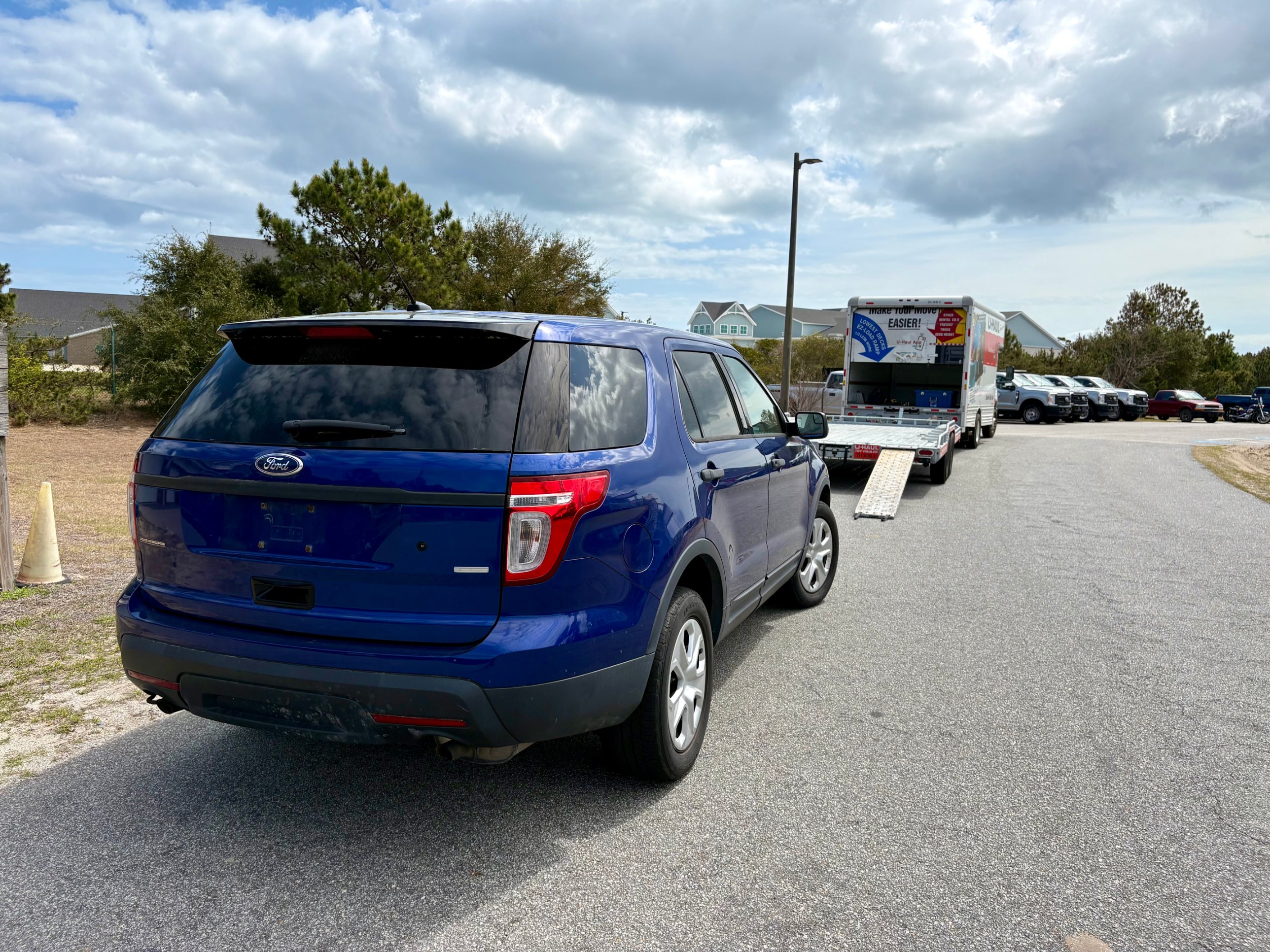 Rear three-quarter view of the blue Ford Explorer with a U-Haul truck and trailer in the background