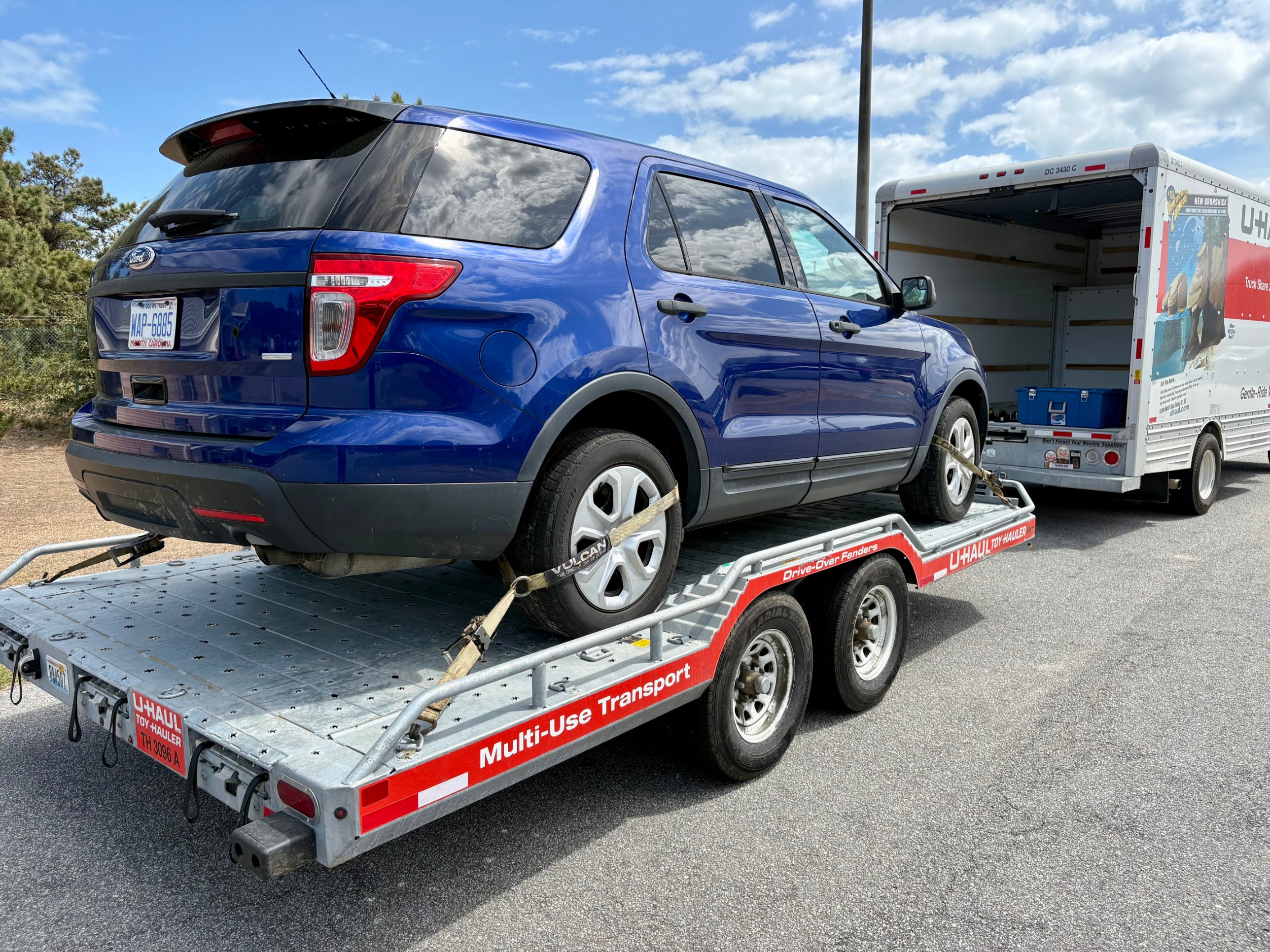 Blue Ford Explorer strapped onto a U-Haul vehicle transport trailer