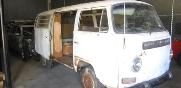 The van with its side door open, showing a stripped, rusted interior, parked in a warehouse beside other cars
