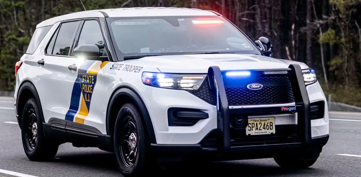 A New Jersey State Police Ford Explorer with its lights on, front view on a wooded highway.