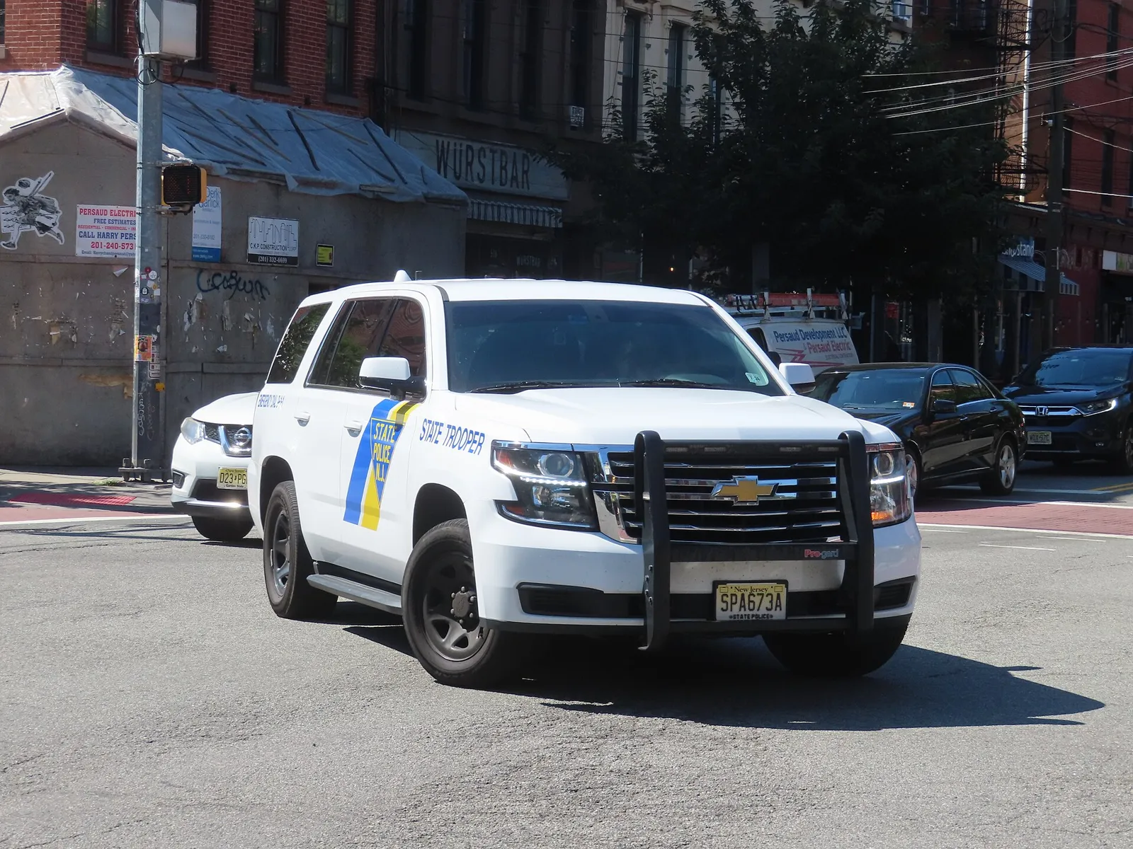 A white New Jersey State Police slicktop Chevrolet Tahoe with a push bumper, front three-quarter view on a city street.
